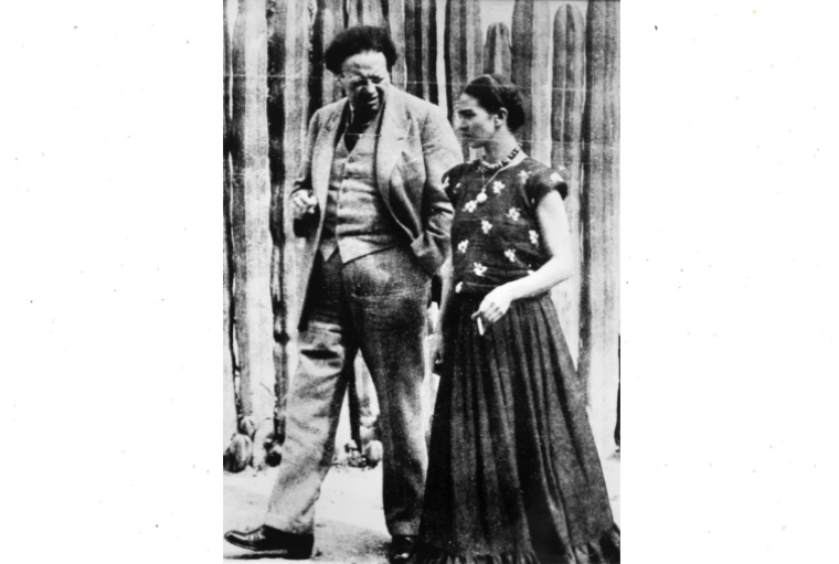 Diego & Frida: Life Chronicles Diego Rivera and Frida Kahlo walking in front of the cactus fence at their studio house